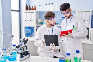 Young couple wearing scientist uniform using touchpad at laboratory