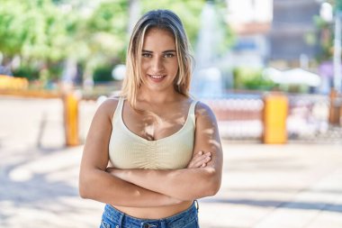 Parkta kollarını kavuşturmuş genç sarışın bir kadın.