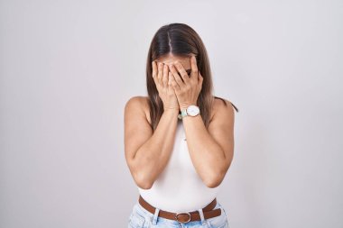 Hispanic young woman standing over white background with sad expression covering face with hands while crying. depression concept. 