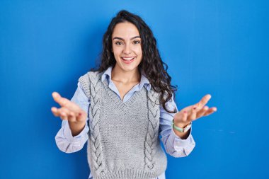 Mavi arka planda duran genç esmer kadın gülümseyerek yardım ve kabullenme eli uzatıyor.. 