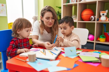 Teacher with boys sitting on table drawing on paper at kindergarten