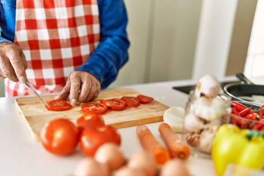 Kıdemli adam mutfakta domates kesiyor.