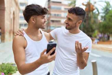 Two hispanic men couple smiling confident using smartphone at street