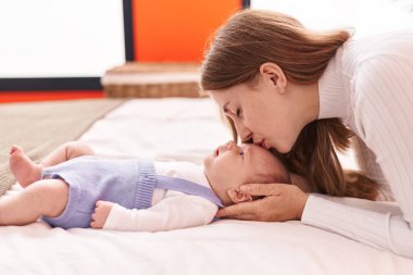 Anne ve oğlu yatakta uzanıp bebeği öpüyor.