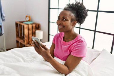 Afrika kökenli Amerikalı bir kadın yatak odasında akıllı telefon kullanıyor.