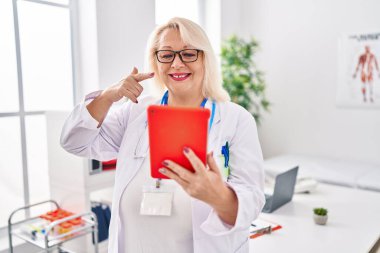 Orta yaşlı, beyaz bir kadın online randevuda çalışıyor mutlu bir şekilde el ve parmağıyla işaret ediyor. 