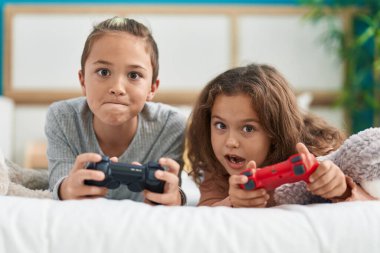 Two kids playing video game lying on bed at bedroom