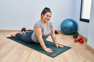 Young beautiful plus size woman smiling confident stretching back at sport center
