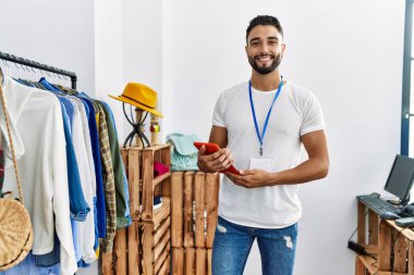Genç Arap esnaf dokunmatik pedini kullanarak giyim mağazasında duruyor.