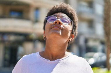 Afro-Amerikalı kadın gülümsüyor. Sokakta nefes alıyor.