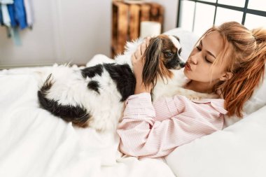 Beyaz bir kadın yatak odasında köpekle yatakta yatıyor.