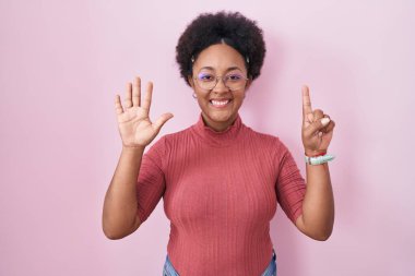 Beautiful african woman with curly hair standing over pink background showing and pointing up with fingers number six while smiling confident and happy. 