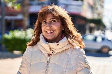 Orta yaşlı bir kadın sokakta kendine güvenerek gülümsüyor.