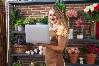 Young beautiful hispanic woman florist smiling confident using laptop at flower shop
