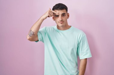 Pembe arka planda duran yakışıklı İspanyol adam alnındaki sivilceden memnun olmadığını gösteriyor, siyah noktalı çirkin bir enfeksiyon. sivilce ve deri problemi 