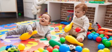 Anaokulunda yerde oturmuş, toplarla oynayan iki sevimli bebek.