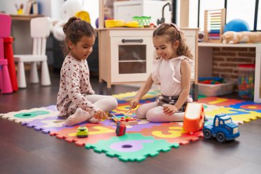 Two kids playing xylophone sitting on floor at kindergarten