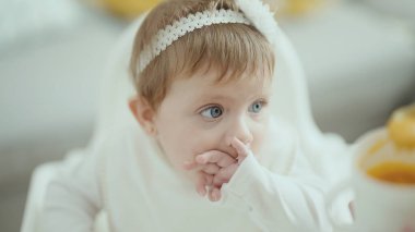 Adorable blonde baby sitting on highchair eating at home