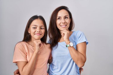 Young mother and daughter standing over white background with hand on chin thinking about question, pensive expression. smiling and thoughtful face. doubt concept. 