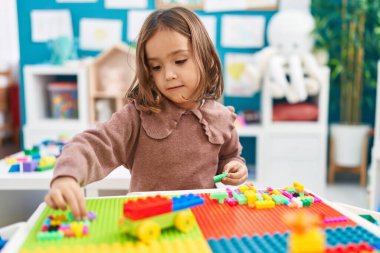 Anaokulundaki masada oturan, inşaat bloklarıyla oynayan sevimli İspanyol kız.