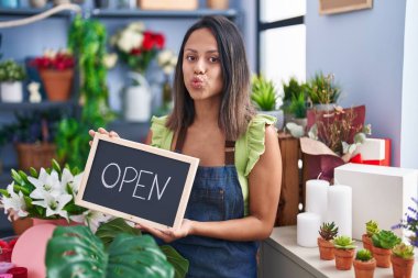Hispanic young woman working at florist with open sign looking at the camera blowing a kiss being lovely and sexy. love expression. 