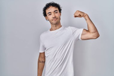 Hispanic man standing over isolated background strong person showing arm muscle, confident and proud of power 