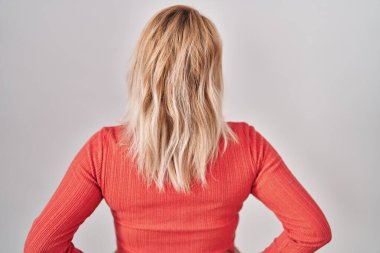 Blonde woman standing over isolated background standing backwards looking away with arms on body 