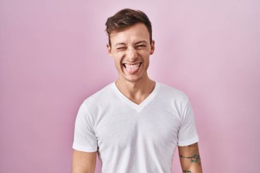 Pembe arka planda dikilen beyaz bir adam komik bir ifadeyle dilini dışarı çıkarıyor. duygu kavramı. 