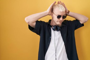 Sarı arka planda duran, güneş gözlüğü takan genç, beyaz bir adam avuçlarında alaycı ve şüpheci bakışlarla tavşan kulağı hareketi yapıyor. Paskalya tavşanı konsepti. 