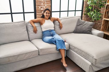 Evdeki kanepede kendinden emin gülümseyen genç İspanyol kadın.