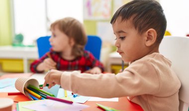 Two kids preschool students sitting on table drawing on paper at kindergarten
