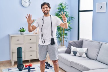 Handsome latin man wearing sportswear at home showing and pointing up with fingers number eight while smiling confident and happy. 