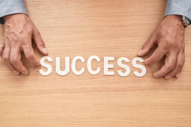 Middle age grey-haired man business worker sitting on table with success word at office