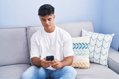 Evdeki kanepede oturan, akıllı telefon kullanan genç bir İspanyol.