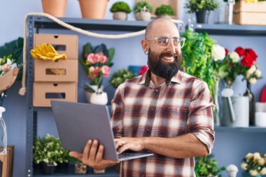 Young bald man florist smiling confident using laptop at flower shop