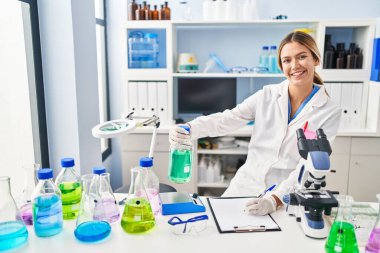 Genç İspanyol kadın bilim adamı. Sıvıyı ölçüyor. Laboratuvarda belgeye yazıyor.