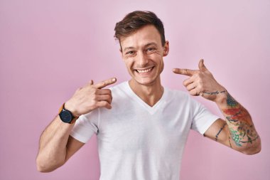 Pembe arka planda duran beyaz bir adam neşeli bir şekilde gülümsüyor ve parmaklarını ve ağzını işaret ediyor. diş sağlığı kavramı. 