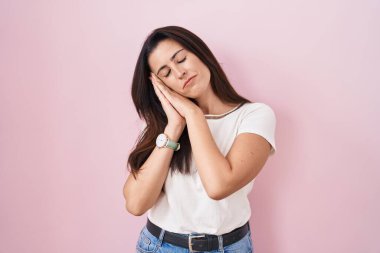 Genç esmer kadın pembe arka planda ayakta uyur. Yorgun düşler kurar, elleriyle poz verir ve gözleri kapalı gülümserdi.. 