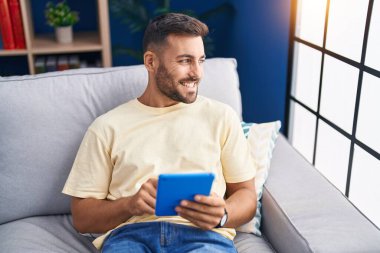 Genç İspanyol adam evdeki koltukta otururken dokunmatik ped kullanıyor.