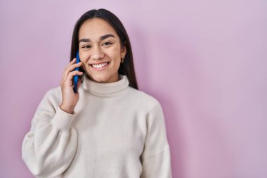 Genç Güney Asyalı kadın akıllı telefondan konuşuyor. Olumlu ve mutlu görünüyor. Kendine güvenen bir gülümsemeyle dişlerini gösteriyor. 