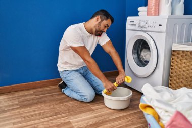 Genç İspanyol adam akıllı telefonda konuşuyor çamaşırhanede paçavraları sıkıyor.