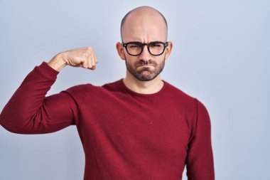 Beyaz arka planda duran sakallı genç kel bir adam gözlüklü güçlü kol kaslı, kendinden emin ve gururlu bir adam. 