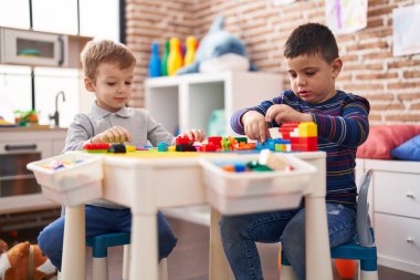 Two kids playing with construction blocks sitting on table at kindergarten