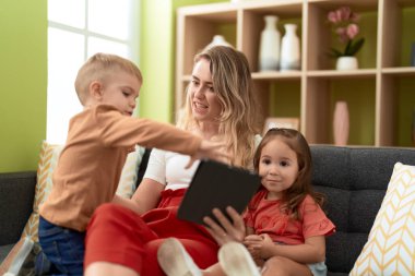 Woman with girl and boy using touchpad sitting on sofa at home
