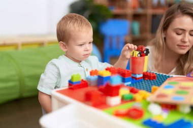Teacher and toddler playing with construction blocks sitting on table at kindergarten