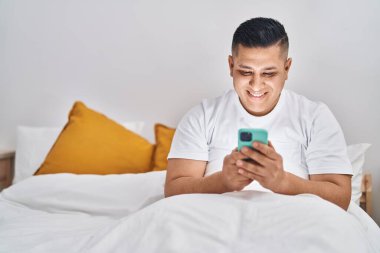 Yatak odasında, akıllı telefon kullanan genç latin adam.