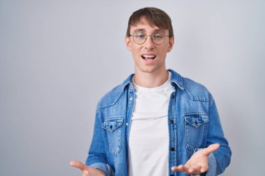 Caucasian blond man standing wearing glasses smiling cheerful with open arms as friendly welcome, positive and confident greetings 