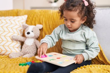 Adorable hispanic girl playing maths game sitting on sofa at home