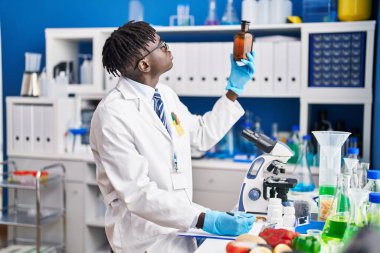 African american man scientist writing report holding bottle at laboratory