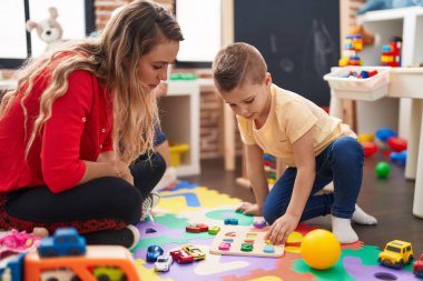 Teacher and toddler playing with maths puzzle game sitting on floor at kindergarten